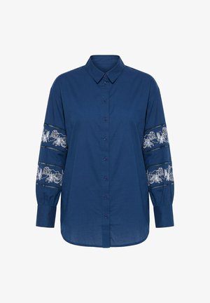 Blauwe blouse met lange mouwen, knopen en kraag, met witte bloemkantpanelen aan de boven- en ondermouwen.