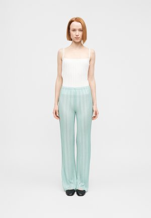 Weißes, geripptes Trägershirt mit dünnen Trägern und hellblaue, plissierte, weit geschnittene Hosen mit elastischem Bund und dezentem Streifenmuster.