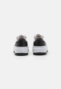 Black and white sneakers with a textured leather upper, raised back, and thick white sole. Distinct logo detail on the heel.