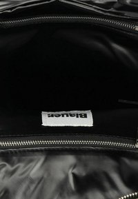 Borsa nera con cerniera, dotata di un'esterno in materiale sintetico lucido. All'interno è foderata in tessuto nero, con un'etichetta bianca che riporta il testo "Blanker".