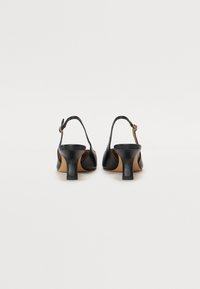 Sorte skinn slingback hæler med rund tå, en lav blokk hæl, og en dekorativ spenne detalj på ankelen.