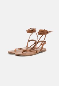 Bruna läder gladiatorsandaler med platt sula, tunna remmar som sveper runt ankeln och minimalistisk design. Inga utsmyckningar eller mönster.