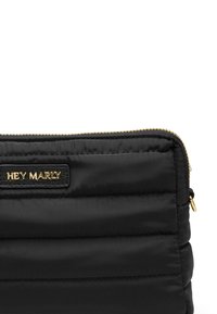 Zwarte, gewatteerde clutch met een gouden rits en een leren label met textuur waarop "HEY MARLY" is gegraveerd.
