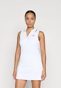 Bílé bezrukávové polo šaty s ribbovanou texturou, límečkem ve tvaru V a černým lemováním. Obsahují malé logo na levé straně hrudi.