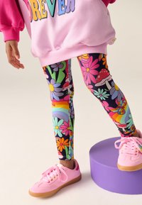 Színes leggings virág- és gombamintákkal, rózsaszín pulóverrel és hozzáillő rózsaszín sportcipővel párosítva. Az anyag puha és rugalmas hatású.