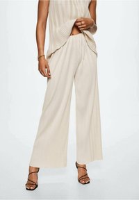 Béžové široké kalhoty s plisovaným designem a texturovaným povrchem. V setu se shodným topem, který zdobí jemné vertikální pruhy.