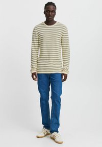 Long-sleeve striped knit shirt in cream with green, blue, and yellow lines, paired with blue jeans and cream sneakers with brown accents.