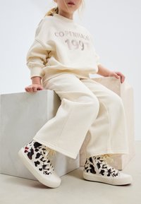 Kremo spalvos džemperis su šviesia siuvinėta užrašu „Kopenhaga 1997“, derinamas su atitinkančiomis laisvalaikio kelnėmis ir aukštakulniais bateliais su karvės raštu.