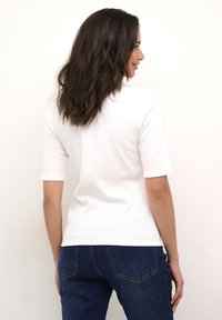 Vit ribbad kortärmad topp sedd bakifrån, ihopparad med blå denimjeans som har två bakfickor och synliga söm detaljer.