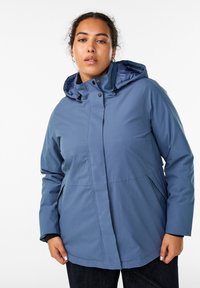 Šviesiai mėlyna, vandeniui atspari striukė su gobtuvu, priekiniais užtrauktukais, snap tipo mygtukais ir šoninėmis kišenėmis. Turi glotnų paviršių ir prigludusią struktūrą.