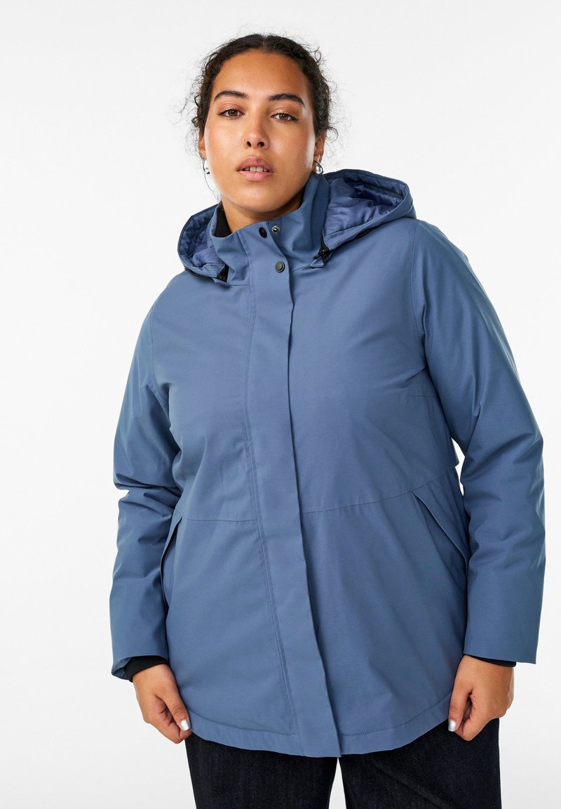 Šviesiai mėlyna, vandeniui atspari striukė su gobtuvu, priekiniais užtrauktukais, snap tipo mygtukais ir šoninėmis kišenėmis. Turi glotnų paviršių ir prigludusią struktūrą.