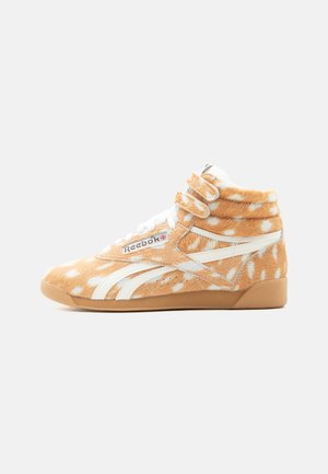 High-top Reebok sneaker met oranje vacht met witte vlekken, witte strepen, dubbele klittenbandriemen en een gumzool.
