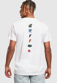 Tricou alb din bumbac, cu mai multe logo-uri, inclusiv un aligator și textul "UF FLORIDA" pe partea din spate, în verde, portocaliu și albastru.