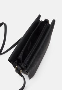 Černá kožená taška přes tělo s tkanou texturou, vybavená zipovou kapsou a nastavitelným popruhem. Hladká podšívka.