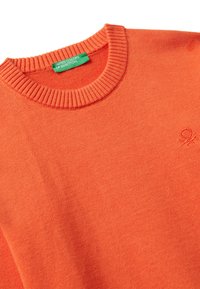 Maglione arancione a collo rotondo lavorato a maglia con collare a coste e piccolo logo ricamato vicino al petto, con etichetta verde United Colors of Benetton.