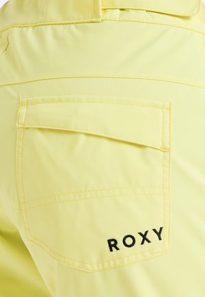 Gelber Stoff mit glatter Textur, ausgestattet mit einer Gesäßtasche und schwarzer "ROXY"-Logo-Stickerei. Einfaches, klares Design mit kontrastierenden Akzenten.