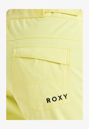 Žltá látka s hladkou textúrou, vybavená zadným vreckom a čiernym stehom loga "ROXY". Jednoduchý, čistý dizajn s kontrastnými detailmi.