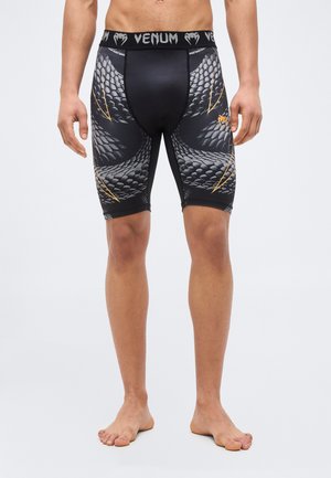 Male model wearing black and gray compression shorts with snake scale pattern and "Venum" logo on waistband and thigh.