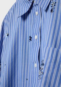 Chemise à rayures verticales bleu et blanc avec des boutons blancs et de petites décorations florales en sequins bleu foncé dispersées.