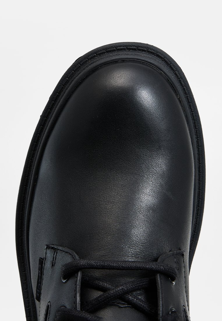 Chaussure en cuir noir au fini lisse, à bout rond et à lacets. Présente des coutures texturées le long du bord et un matériel minimal.