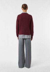 Burgundowy sweter dzianinowy nałożony na szaro-biały pasiasty T-shirt, w połączeniu z szerokimi spodniami dżinsowymi w kolorze szarym. Teksturowany materiał i luźny krój.