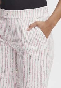 Witte, gestreepte broek met verticale strepen in roze en zwart. Het materiaal is lichtgewicht met een gladde textuur; inclusief zijzakken.