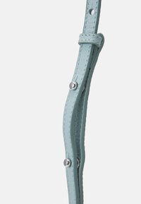 Cinturino in pelle azzurro chiaro con bottoni a pressione argentati e dettagli di cucitura su uno sfondo bianco semplice.