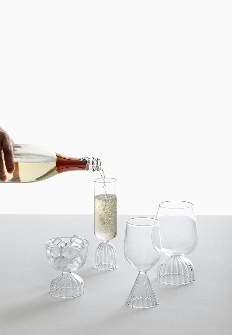 Przezroczysta szklarnia z falistą podstawą; zawiera wysoką flutę, okrągły kielich i miskę na lód. Błyszczący napój wlewany jest do fletu.