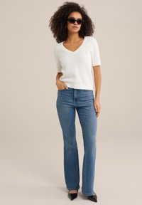 Vit stickad tröja med V-ringning och korta ärmar, i kombination med blå raka jeans och svarta spetsiga klackskor.