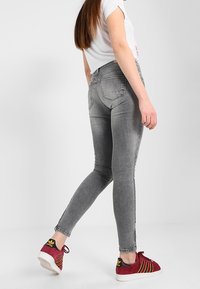 Vaqueros ajustados grises de mezclilla, con una cintura alta, cinco bolsillos y un ligero desgastado, combinados con zapatillas rojas y amarillas.