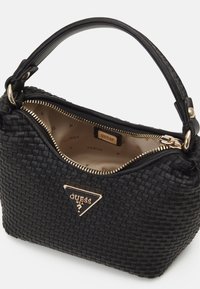 Sac à main en cuir tissé noir avec une poignée unique, une fermeture éclair dorée et un logo triangulaire Guess à l'avant, présenté partiellement ouvert.