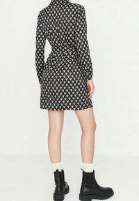 Černé šaty s bílými vzory srdcí, dlouhými rukávy, s páskem v pase a rovného střihu. V kombinaci s černými kotníkovými botami a krémovými ponožkami.