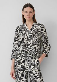 Zwart-witte blouse met patroon, met een V-hals, lange mouwen en een relaxte pasvorm, gecombineerd met een bijpassende broek met een vergelijkbaar ontwerp.