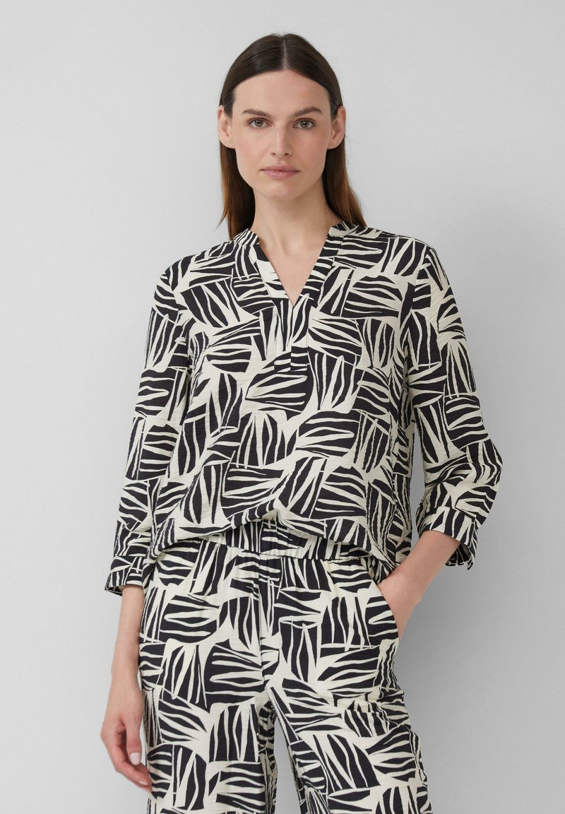 Zwart-witte blouse met patroon, met een V-hals, lange mouwen en een relaxte pasvorm, gecombineerd met een bijpassende broek met een vergelijkbaar ontwerp.