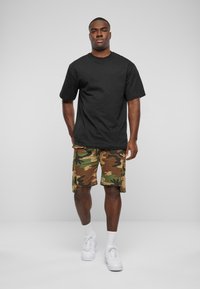 Sort kortærmet t-shirt parret med camouflage cargo shorts. Shortsene har sidelommer og en afslappet pasform. Bæres med hvide sneakers.