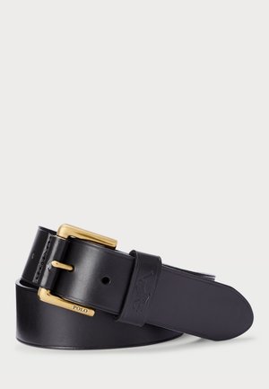 Cintura in pelle nera con fibbia dorata e logo impresso vicino alla fibbia, arrotolata su uno sfondo bianco.