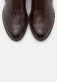 Brązowe skórzane botki za kostkę o gładkiej fakturze, spiczastym nosku i minimalnych detalach przeszycia wzdłuż podeszwy.