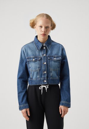 Giacca di jeans blu cropped con colletto a punta, due tasche sul petto e chiusure con bottoni argentati. Tessuto texturizzato, abbinata a pantaloni neri.