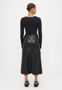 Fekete, hosszú ujjú body, amihez térd alatt végződő, sima textúrájú és finom varrásokkal ellátott fekete bőr szoknya tartozik. Tömör fekete cipők.