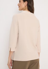 Ljus beige ribbad topp med krage och trekvartsärmar, med sidoflikar och en slät textur.