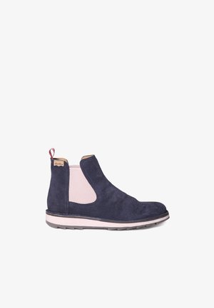 Bottine en suede bleu marine avec des panneaux latéraux élastiques, surface texturée et un accent rose. Dispose d'une semelle marron et blanche avec un léger motif.
