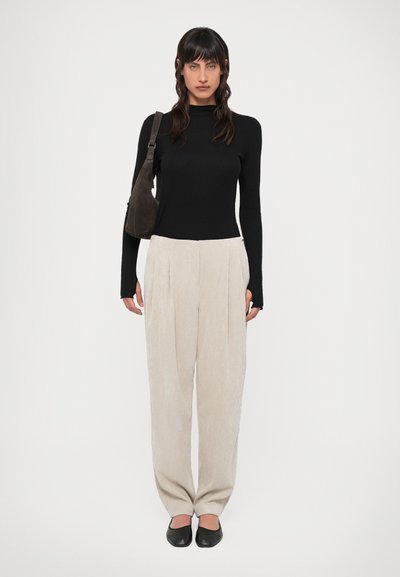 Maglietta nera a maniche lunghe, pantaloni beige plissettati, borsa scura e scarpe ballerine nere. Vestibilità slim, texture a coste sulla maglietta e tessuto morbido nei pantaloni.