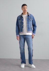 Denim jakk, millel on pruun krae, koos valge T-särgi ja helesiniste teksadega, mille külgedel on mustrid. Valged tennisetossud.
