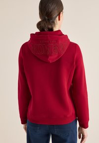 Czerwony hoodie z kapturem na sznurki. Na plecach haftowany napis "SPOKOJNIE I WYGODNIE MOMENT". Miękki materiał, luźny krój, ściągacze przy rękawach.