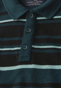 Mörkgrön och svart randig polo med texturerad tyg, utrustad med knappslå och tre mörka knappar, samt en etikett som visar varumärket.