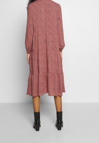 Feminint rosa klänning med ett spritt svart mönster, långa ärmar, lagerdesign och utsvängd nederdel. Bärs med svarta ankelstövlar.