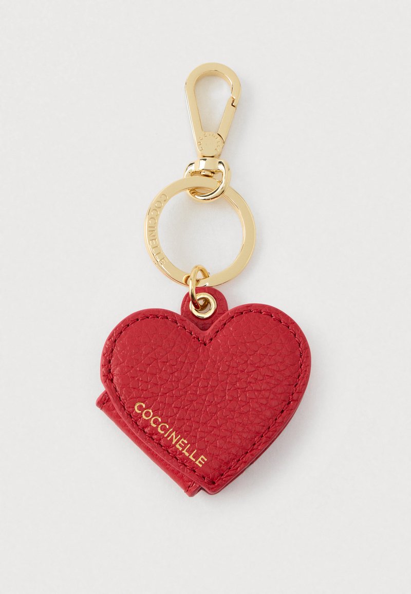 Breloc cu formă de inimă din piele roșie texturată, cu un terminal și inel auriu; cuvântul "COCCINELLE" embosat în aur pe inimă.