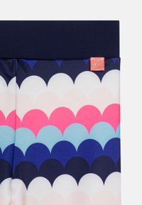 Leggings colorés arborant un motif ondulé dans des nuances de rose, de bleu et de marine, avec une taille unie marine et une petite étiquette décorative.