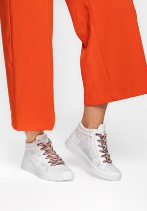 White high-top sneakers with perforated sides, colorful rainbow laces, and side zippers worn with bright orange cropped pants.