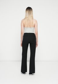Black flared pants with a smooth texture and side pockets, paired with a fitted gray strapless top. Background is plain white.